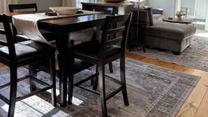 A dining area with a wooden table and chairs, a rug, and a sofa in a room with light-colored walls and a wooden floor. - 12 Mins from Beach - A Quiet, Immaculate space (Norwell)
