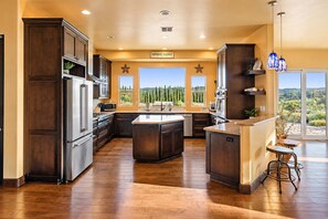 A spacious kitchen with dark wood cabinets, stainless steel appliances, and a large island. - Vino On Vineyard by LUX Retreats Paso (Paso Robles)