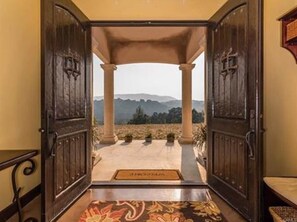 A grand entrance with a view of mountains, a covered area with columns, and a patterned floor. - Vino On Vineyard by LUX Retreats Paso (Paso Robles)