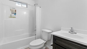 A bathroom with a white toilet, a bathtub, and a sink with a dark vanity. - Brand New 3 bed house in central San Benito with AC, WiFi, and digital features (San Benito)