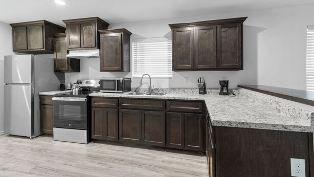 A modern kitchen with dark wood cabinets, a stainless steel refrigerator, a built-in oven, a microwave, and a granite countertop. - Brand New 3 bed house in central San Benito with AC, WiFi, and digital features (San Benito)
