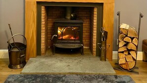 A cozy fireplace with a wood-burning stove, a framed picture above it, and decorative wall art. - Charming 2-bedroom cottage in Kingsbarns  (Kingsbarns)
