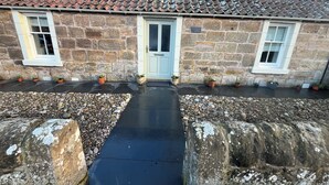 A stone building with a tiled roof, a central entrance, and potted plants along the pathway. - Charming 2-bedroom cottage in Kingsbarns  (Kingsbarns)