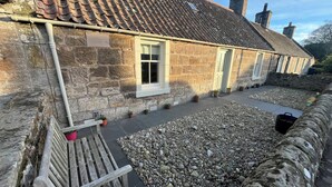 A stone building with a tiled roof, a bench, and a pebbled area. - Charming 2-bedroom cottage in Kingsbarns  (Kingsbarns)