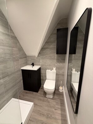 Un baño moderno con un lavamanos blanco, armarios negros, un inodoro blanco y un espejo grande.