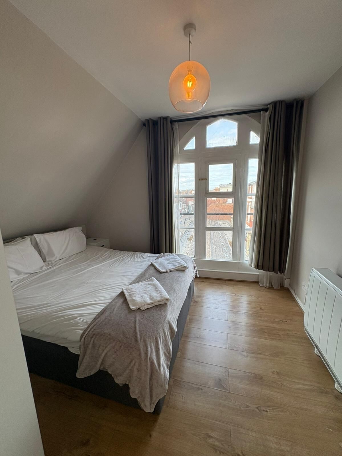 A bedroom with a large bed, a window with curtains, and a hanging light fixture.