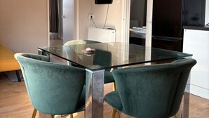 Een moderne eetruimte met een glazen tafel en teal gekleurde stoelen, een zwarte koelkast en een hangende televisie.