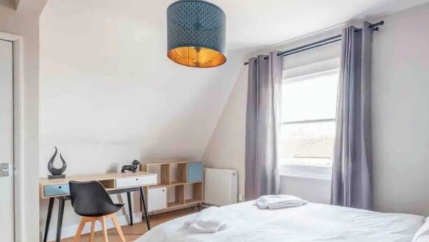 Een slaapkamer met een bed, bureau, stoel en een raam met gordijnen.