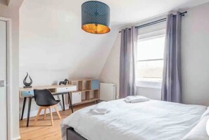 Un dormitorio con cama, escritorio, silla y ventana con cortinas.