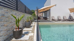 A pool area with lounge chairs and umbrellas, a stone wall, and potted plants. - Apartment BARBARA with private pool (Malinska)
