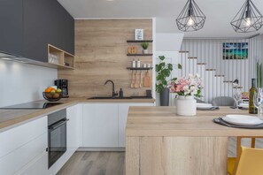 Una cocina moderna con detalles de madera, un horno empotrado y una zona de comedor con mesa y sillas de madera.