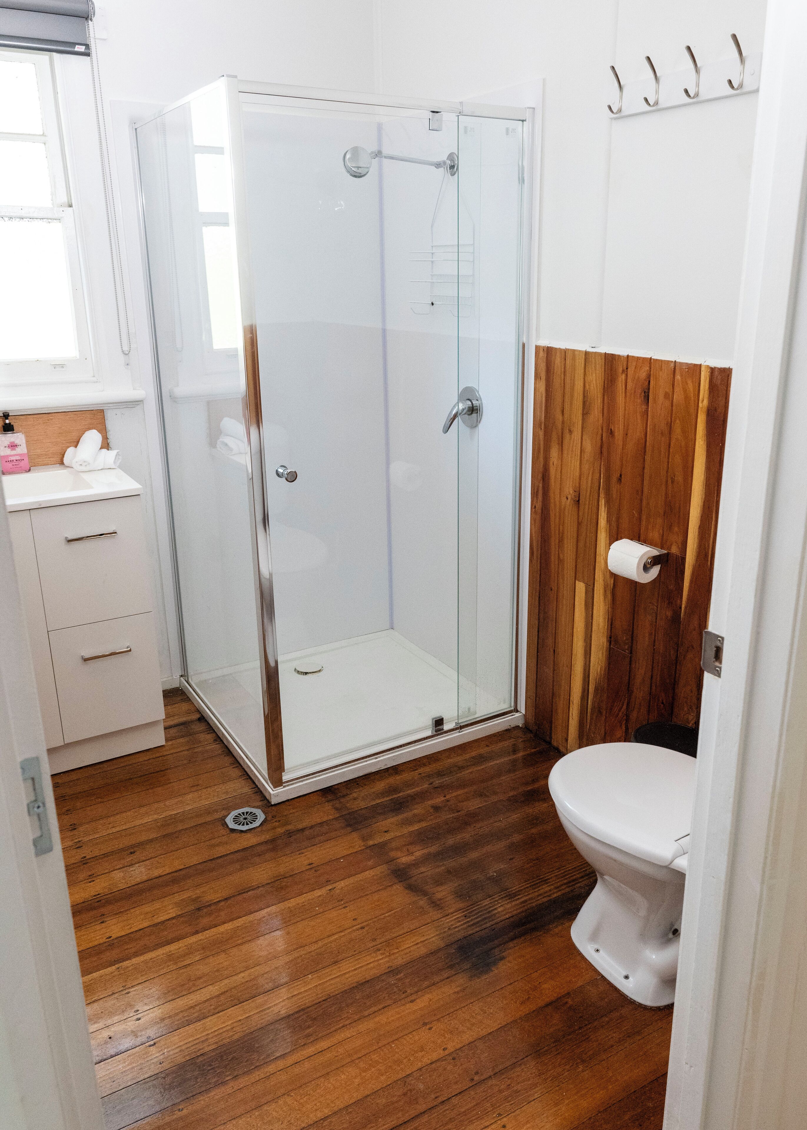 Un bagno con box doccia in vetro, pavimento in legno, WC e lavabo con specchio.