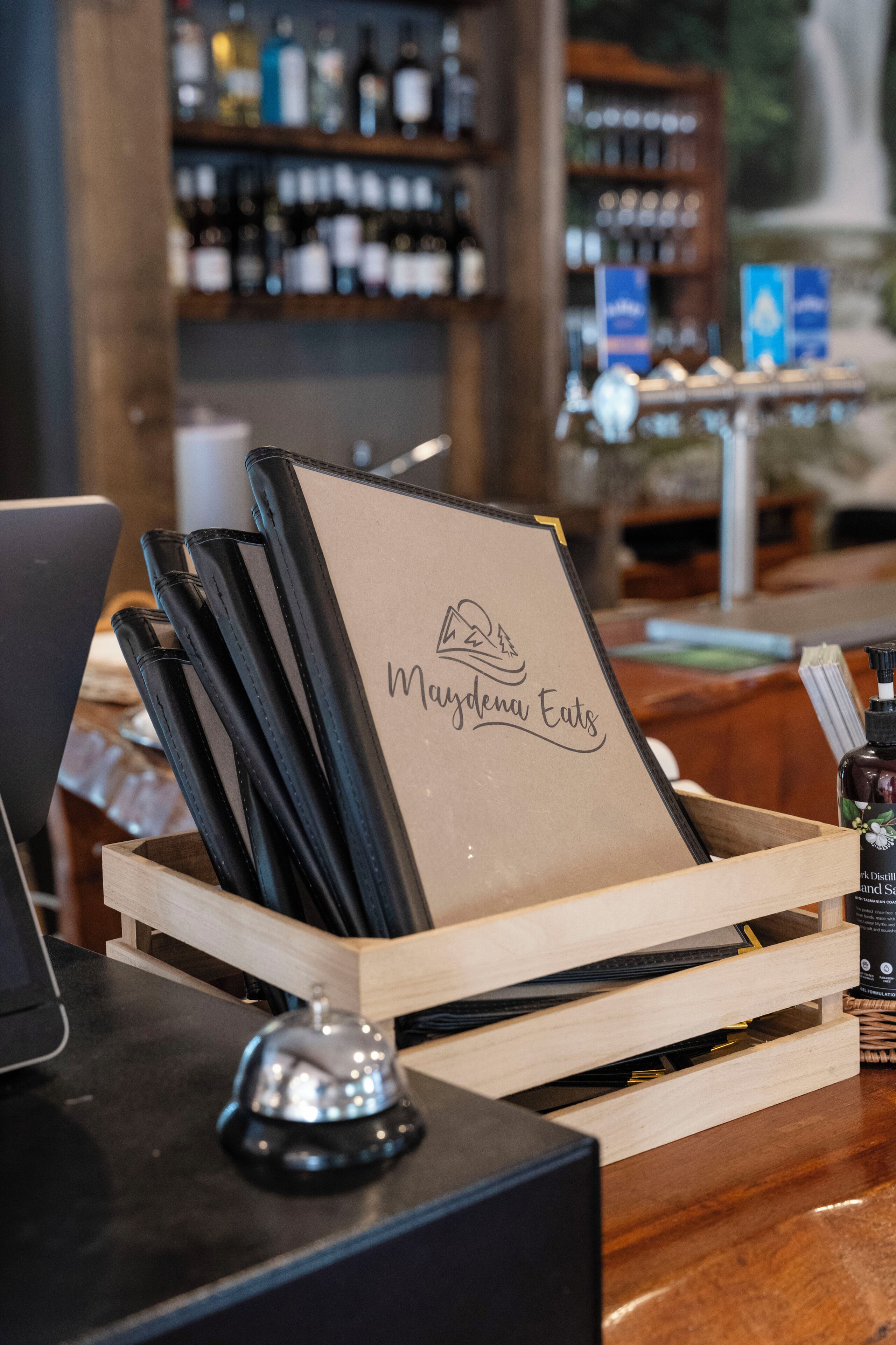 A wooden crate with black notebooks and a menu board labeled "Maydenu Eats" in a restaurant setting.