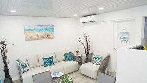 A modern living room with a beige sofa, a dining table, and decorative plants. -  Cosy one bedroom condo in Holetown, St. James with pool access!! (Holetown)