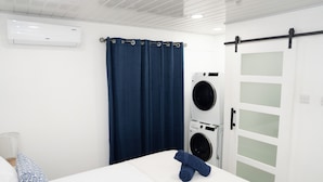 A hotel room with a bed, a blue towel, a washing machine, and a sliding door. -  Cosy one bedroom condo in Holetown, St. James with pool access!! (Holetown)