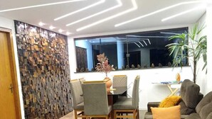 A modern living room with a sofa, a dining table with chairs, and a decorative wall. - Pousada château Lumière  (Itaara)