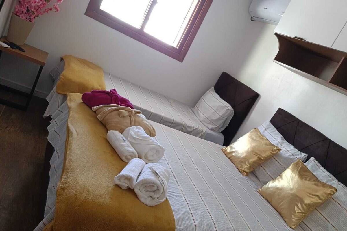 A hotel room with a bed, a window, a bedside table, and a wall-mounted shelf.