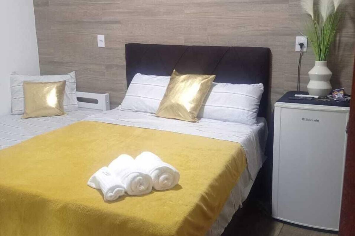 A hotel room with a bed, a bedside table, an air conditioner, and a minibar.