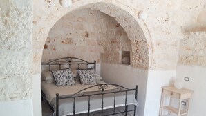 A bedroom with a stone wall, a bed with striped bedding, and a small wooden nightstand. - Trullo near Ostuni quiet with fenced heated pool with Starlink wifi (Latiano)