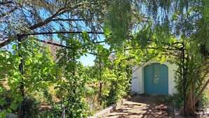 A pathway leading to a building with a green door, surrounded by lush greenery and trees. - Trullo near Ostuni quiet with fenced heated pool with Starlink wifi (Latiano)