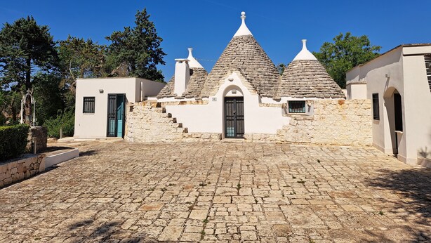 A traditional stone building with a steeply pitched roof, a central entrance, and a cobblestone courtyard. - Trullo near Ostuni quiet with fenced heated pool with Starlink wifi (Latiano)