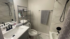 A bathroom with a white sink, toilet, and shower. There is a towel rack with a striped towel hanging on it.