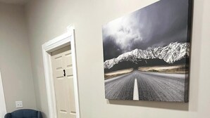 A living room with a beige sofa, brown leather cushions, a blue armchair, and a large painting of a snowy mountain road.