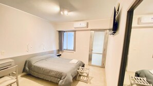 Une chambre à coucher comprenant un lit, un bureau, une chaise, une fenêtre et un appareil de climatisation.