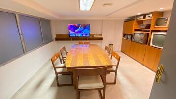 A dining area with a wooden table and chairs, a television on the wall, and a kitchen area with wooden cabinets and appliances.