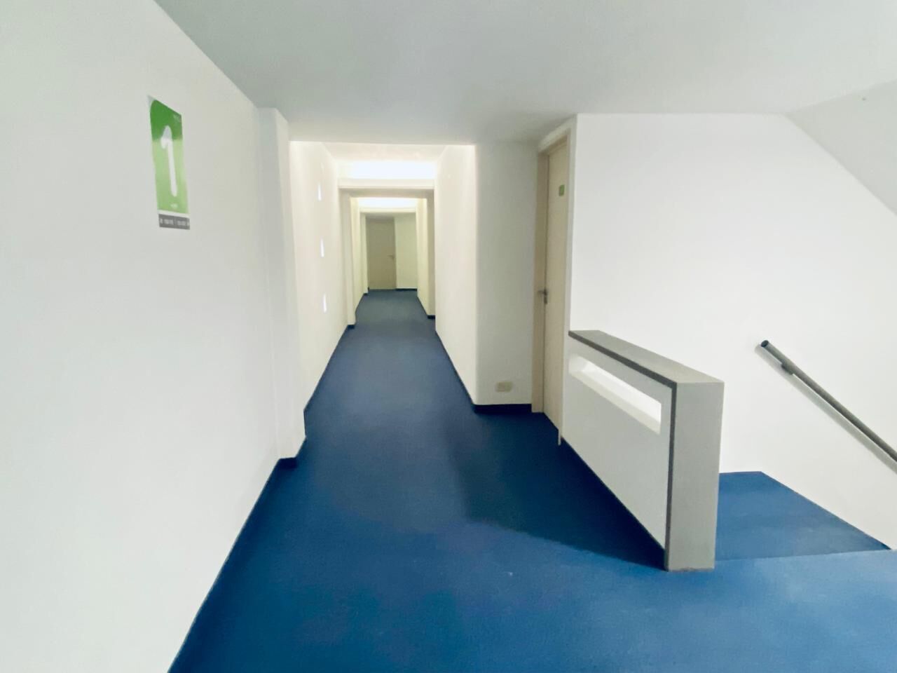 A hallway with a blue carpet, white walls, and a door at the end.