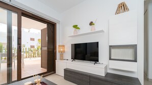 Un salon moderne doté d’un téléviseur à écran plat, de meubles en bois et d’une porte-fenêtre coulissante donnant sur un espace extérieur.
