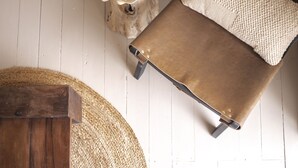 Una mesa de madera, un tapete redondo tejido y una silla de cuero marrón con un cojín texturizado.
