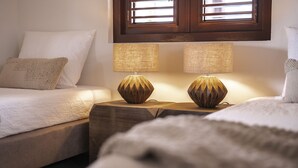 Un dormitorio con dos camas, cada una con un almohadón blanco y una manta texturizada. Entre las camas hay dos mesitas de noche con lámparas.