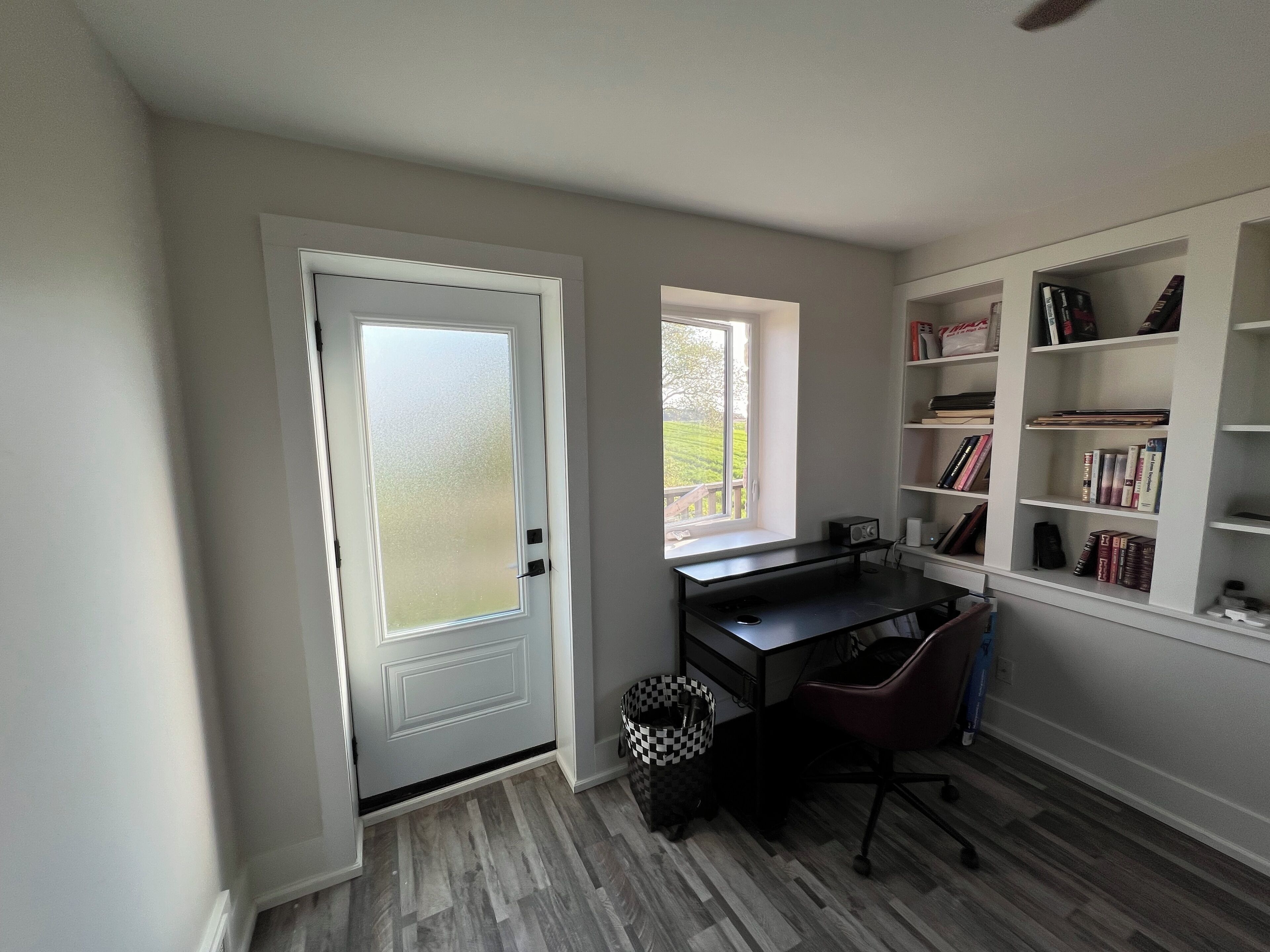 Una sala de estudio con escritorio, silla, estantería y ventana con vista a zonas verdes.