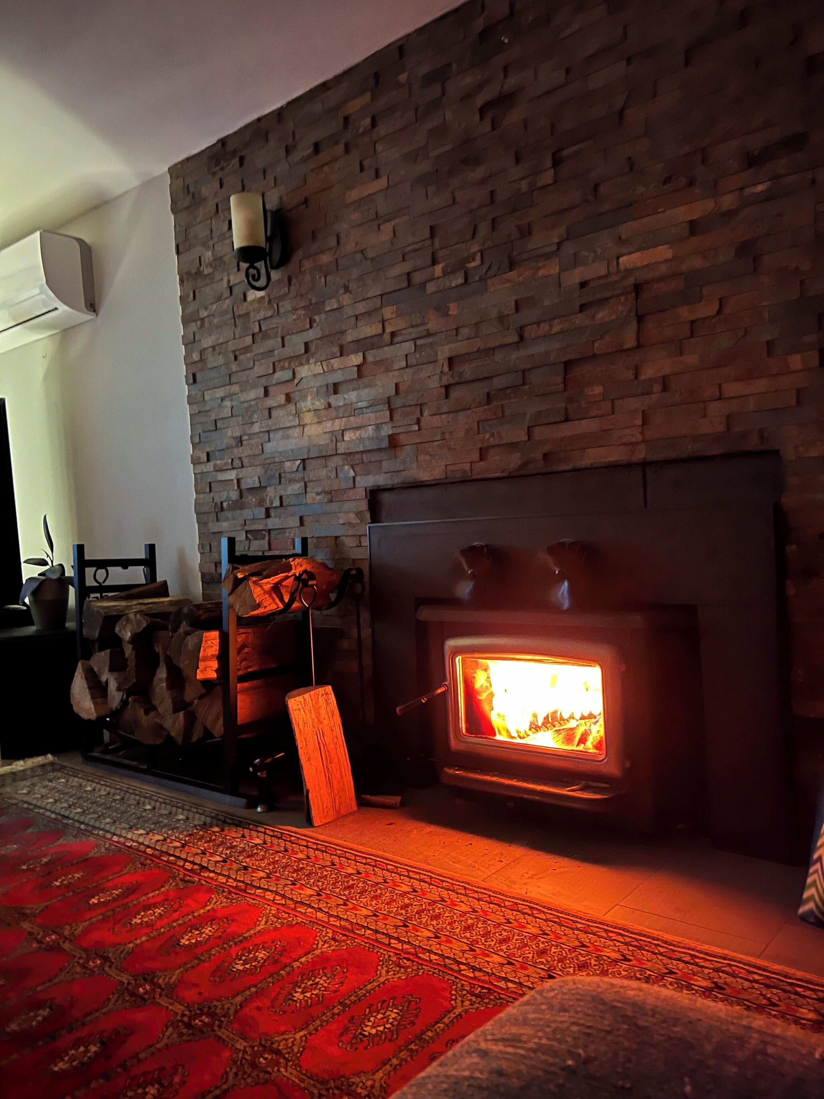 A cozy living room with a stone wall, a fireplace, and a patterned rug.