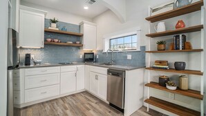 A modern kitchen with white cabinetry, blue backsplash, wooden shelves, and a dishwasher.