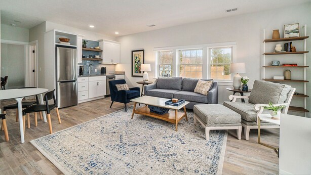 A modern living room with a gray sofa, a coffee table, and a dining area with a white table and chairs.