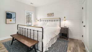 A bedroom with a bed, bedside table, bench, and artwork.