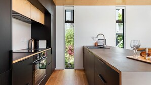 Une cuisine moderne avec des meubles de couleur sombre, un plan de travail en bois et une vue sur la verdure à l’extérieur.