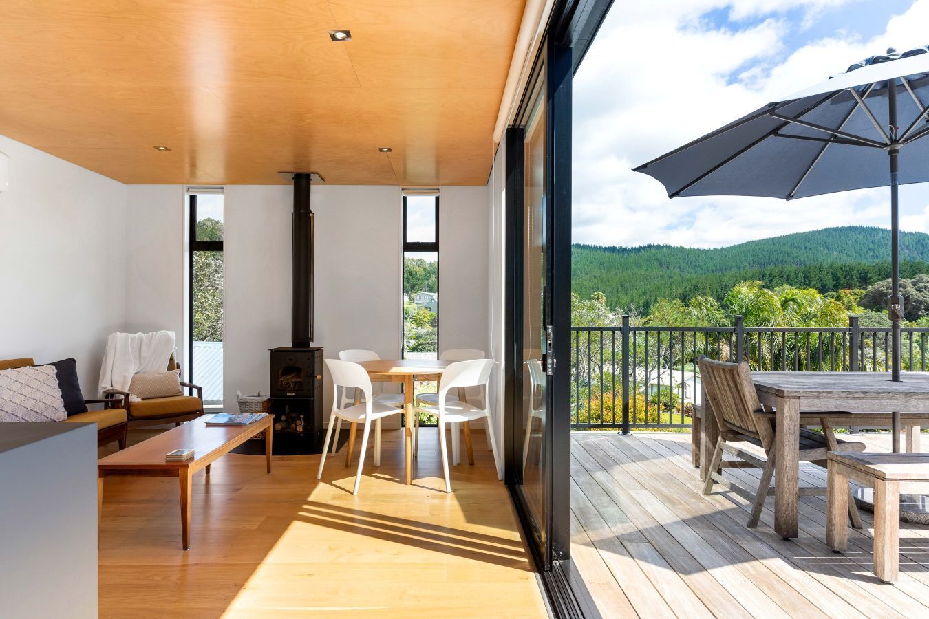 Un interior moderno con techo de madera, chimenea, comedor con sillas y balcón con mesa y sombrilla.