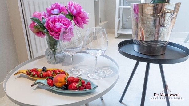 A table with a fruit platter, two wine glasses, a vase with pink flowers, and a champagne bottle in a bucket. - De Montescal - A/C & Hot Tub Studio (Paris)