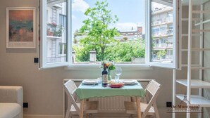 A dining area with a table set for two, a window with an open view of a tree and buildings, and a framed artwork on the wall. - De Montescal - A/C & Hot Tub Studio (Paris)