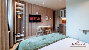 A modern hotel room with a bed, a desk, a chair, a TV mounted on the wall, and a kitchenette. - De Montescal - A/C & Hot Tub Studio (Paris)