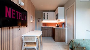 A compact kitchen with wooden cabinets, a white countertop, and a dining area with a white table and chairs. - De Montescal - A/C & Hot Tub Studio (Paris)