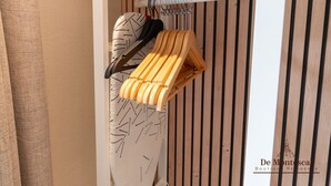 A closet with wooden slats, a hanging rack, and a white ironing board. - De Montescal - A/C & Hot Tub Studio (Paris)