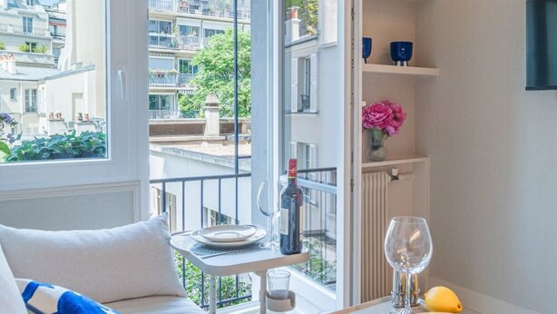 A modern apartment with a balcony, a dining area with a table set for two, and a view of the cityscape. - De Montescal - Studio (Paris)