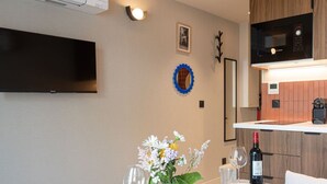 A modern hotel room with a flat-screen TV, a small dining table set with plates and glasses, a vase with flowers, and a bottle of wine. - De Montescal - Studio (Paris)