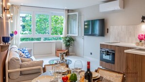 A modern kitchen with a built-in oven, a dining area with a table set for two, and a large window offering a view of greenery. - De Montescal - Hot tub & A/C Apartment (Paris)