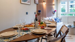 A dining table set with plates, glasses, and a bottle of wine, with a cityscape painting and a poster on the wall. - De Montescal - Hot tub & A/C Apartment (Paris)