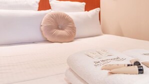 A neatly made bed with white linens and a beige accent pillow, a folded towel with text, and a bottle of lotion on the bed.